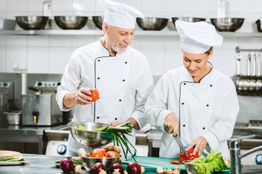 gülümseyen kadın ve erkek şefler kruvaze ceketler ve Restoran mutfağında yemek şapkalar