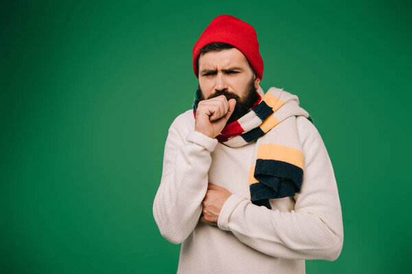 ill man in hat and scarf coughing isolated on green