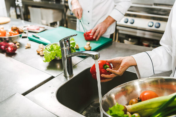 cropped view of female chef washing pepper in restaurant kitchen