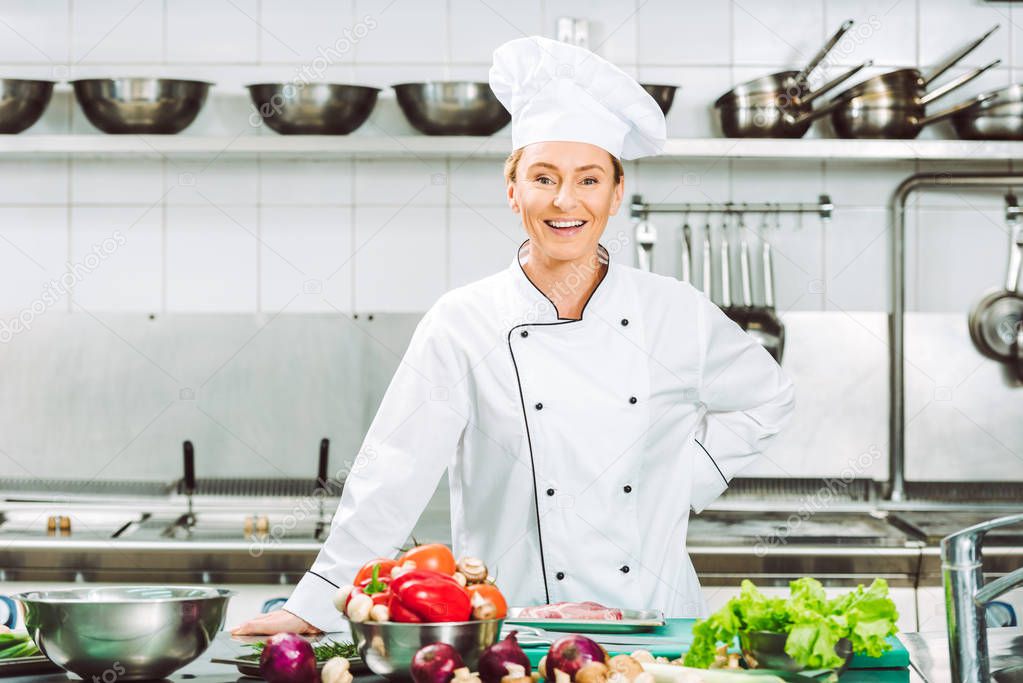 beautiful happy female chef in uniform looking at camera during cooking in restaurant kitchen