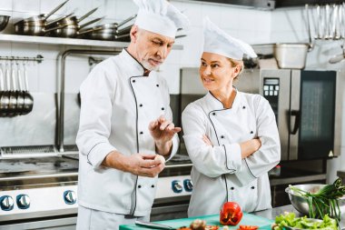 Restoran mutfakta yemek yaparken konuşmayı üniformalı kadın ve erkek şefler