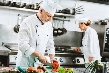 selective focus of male and female chefs in uniform preparing food in restaurant kitchen clipart