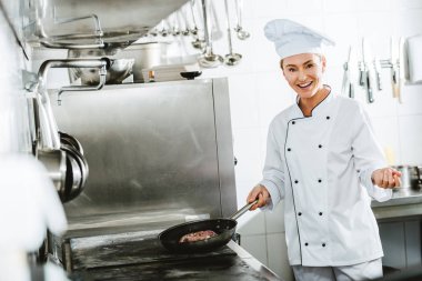 tek tip kameraya bakarak et Restoran mutfakta yemek yaparken güzel gülümseyen kadın şef