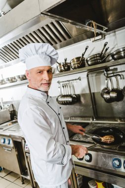 male chef in uniform cooking meat in restaurant kitchen clipart