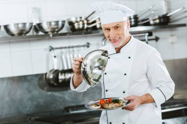 kameraya bakarak ve kubbe et yemek restoran mutfak ile tepsi hizmet tutan üniformalı yakışıklı erkek Şef