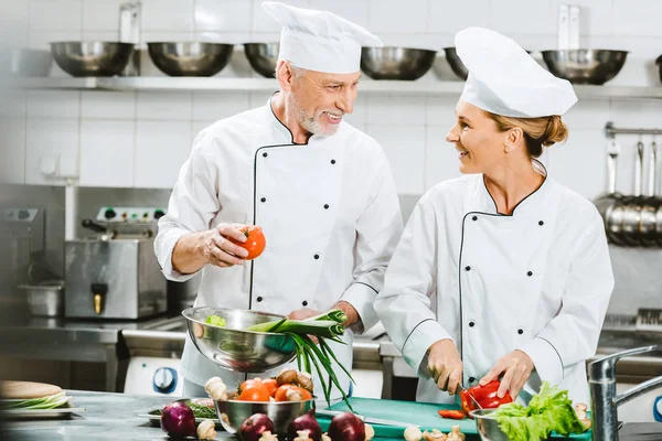 微笑的女性和男性厨师在餐厅厨房做饭时 穿着制服互相看着对方 — 图库照片
