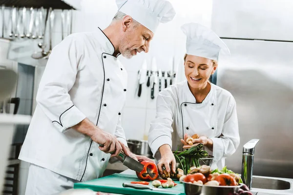 female and male chefs in uniform and hats cooking in restaurant kitchen