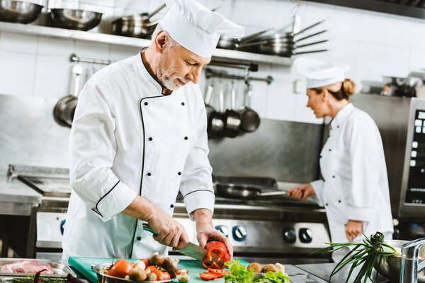 selective focus of male and female chefs in uniform preparing food in restaurant kitchen