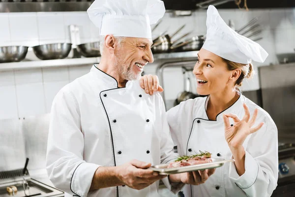 Chef Masculino Apresentando Prato Carne Para Colega Sorrindo Mostrando Sinal — Fotografia de Stock