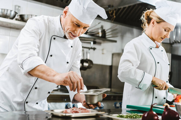 focused male and female chefs in uniform preparing food in restaurant kitchen