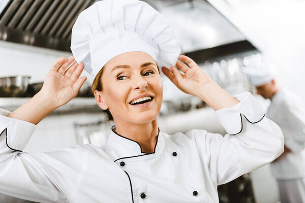 beautiful smiling female chef adjusting cap in restaurant kitchen