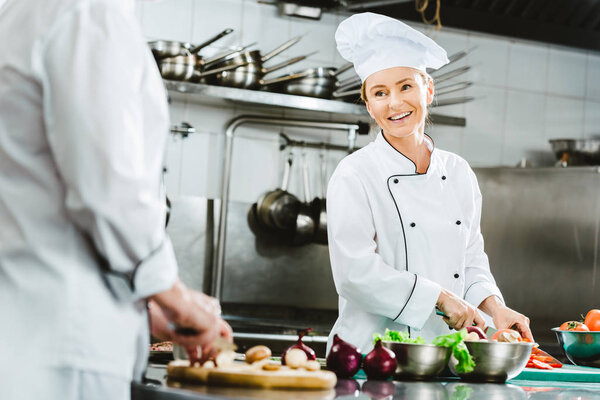 beautiful female chef in uniform smiling while cooking in restaurant kitchen