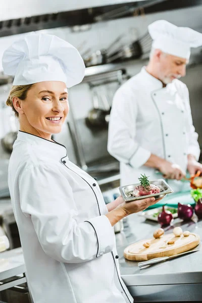 Köchin Uniform Hält Fleischgericht Auf Teller Männlicher Kollege Kocht Hintergrund — Stockfoto