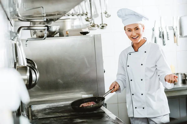 Hermosa Mujer Sonriente Chef Uniforme Mirando Cámara Mientras Cocina Carne — Foto de Stock