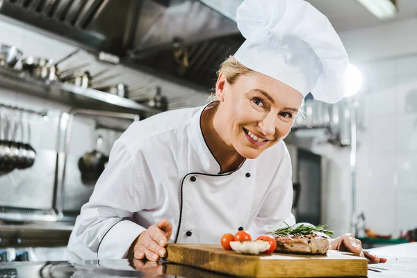 美丽的女厨师在制服举行肉牛排与迷迭香在木板在餐厅厨房 — 图库照片