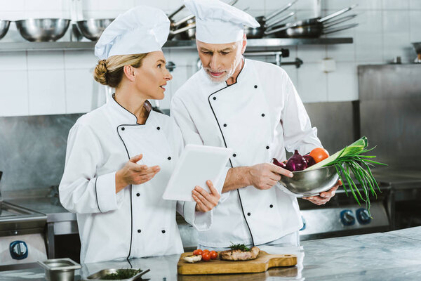 female and male chefs in iniforms using digital tablet during cooking in restaurant kitchen