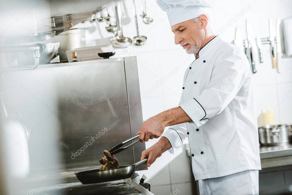 male chef roasting meat steak in restaurant kitchen