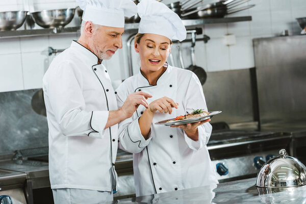 female and male chefs in uniform with meat steak on plate in restaurant kitchen
