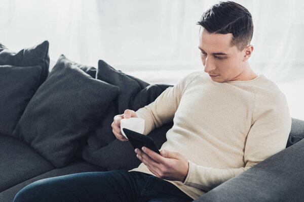 handsome man holding cup and studing with ebook at home
