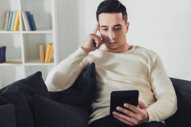 handsome man studing with ebook while sitting on sofa  clipart