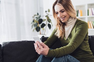 kanepede otururken Smartphone tutan mutlu kadın 