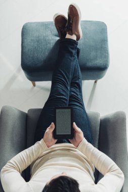 top view of man holding e-reader while sitting in armchair  clipart