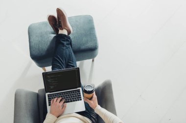 Kağıt bardak tutan ve ekran bilgisayar kodu içeren dizüstü kullanarak insanın üstten görünüm