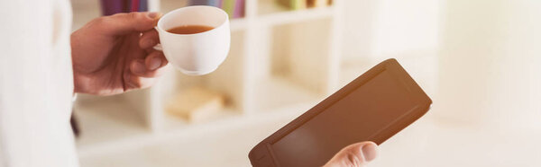 cropped view of e-reader and cup of tea in hands of man 