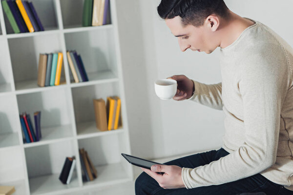 Красивый мужчина с книгой в руках, держа чашу с напитком
