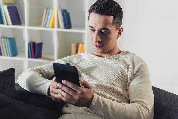 красивый мужчина, сидящий дома с электронной книгой
 