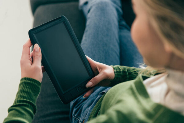 избирательный фокус женщины, держащей электронную книгу с чистым экраном, сидя на диване
 