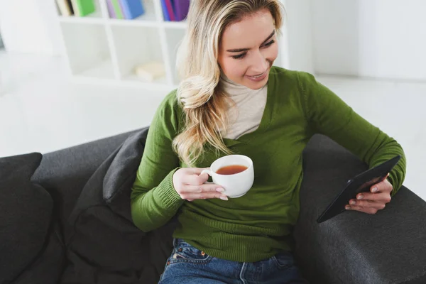 自宅の電子書籍で勉強しながらお茶とカップを保持している魅力的な女性 — ストック写真