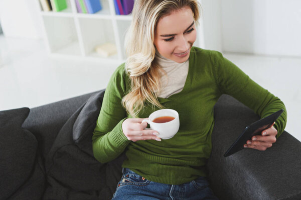 attractive woman holding cup with tea while studing with e-book at home 