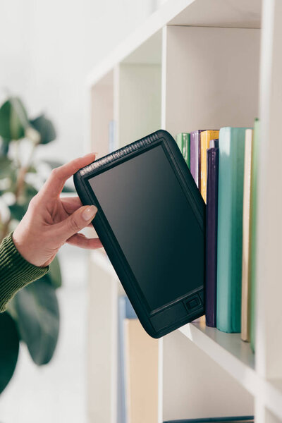 cropped view of woman taking ebook with blank screen from bookshelf