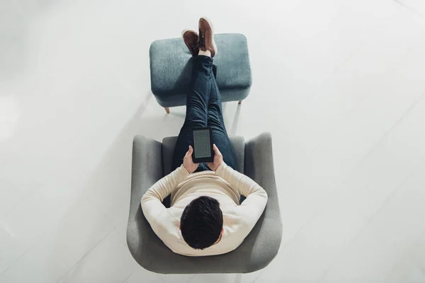 top view of man reading e-book while sitting in armchair at home