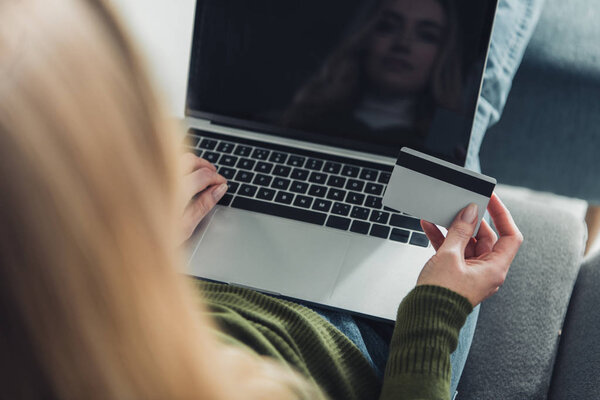 selective focus of woman using laptop with blank screen while holding credit card