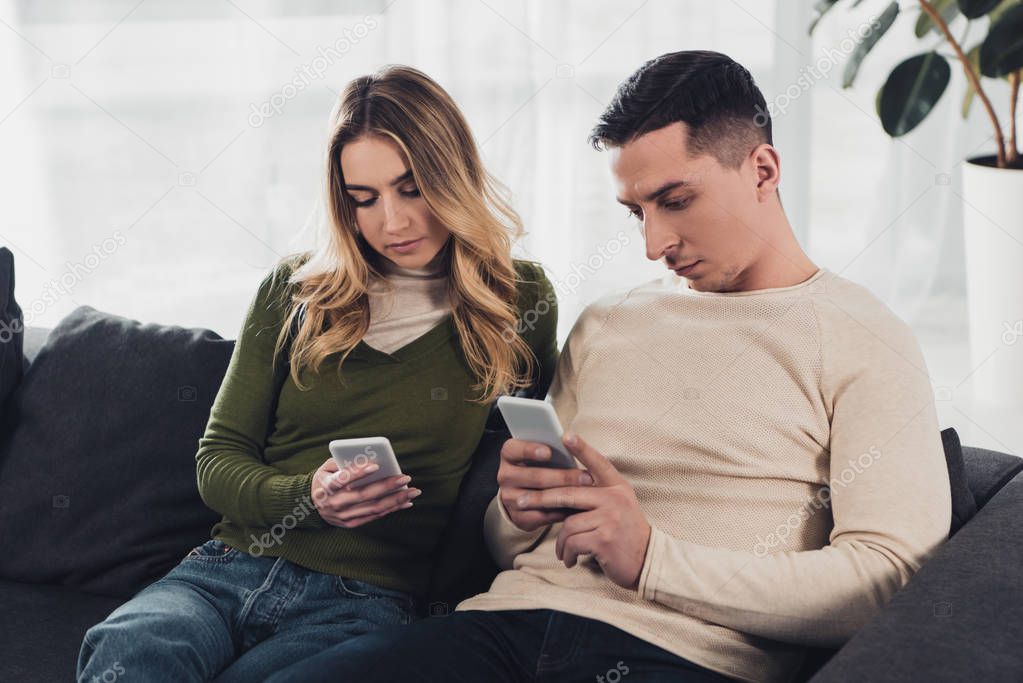 man and woman using smartphones while sitting on sofa at home