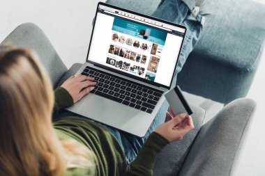 kredi kartı tutan ve amazon Web ekran ile dizüstü bilgisayar kullanarak bir kadın görünümünü kırpılmış 