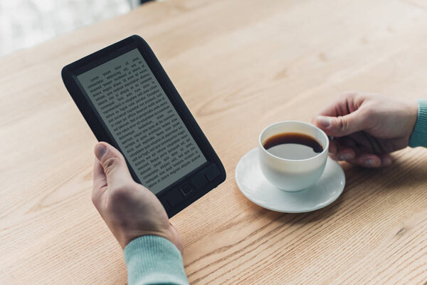 обрезанный вид человека, держащего чашку чая возле электронной книги во время обучения у себя дома
