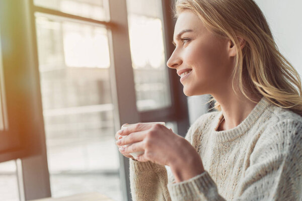 attractive woman holding cup of tea and looking at window 