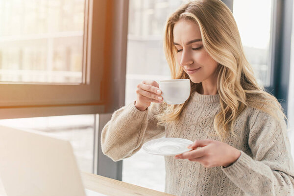 attractive woman smiling with closed eyes and holding cup with tea