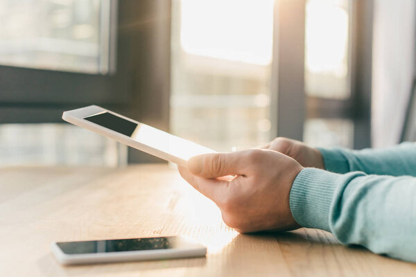 cropped view of man holding digital tablet near smartphone on table