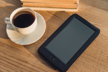 black e-reader with blank screen lying near cup with coffee on table  clipart