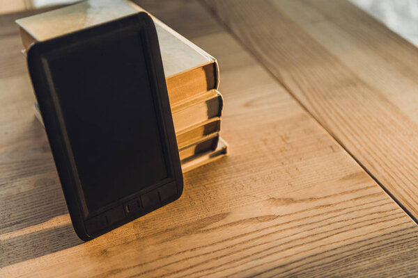 e-reader with blank screen near paper books on wooden table