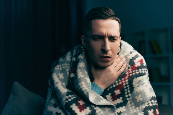  man wrapped in blanket having sore throat at home