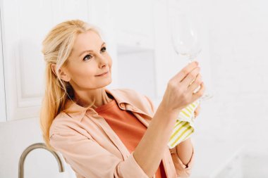 Pleased senior woman wiping wineglass with dishcloth clipart