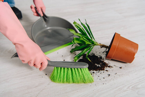 Partial view of woman in pink rubber gloves sweeping floor
