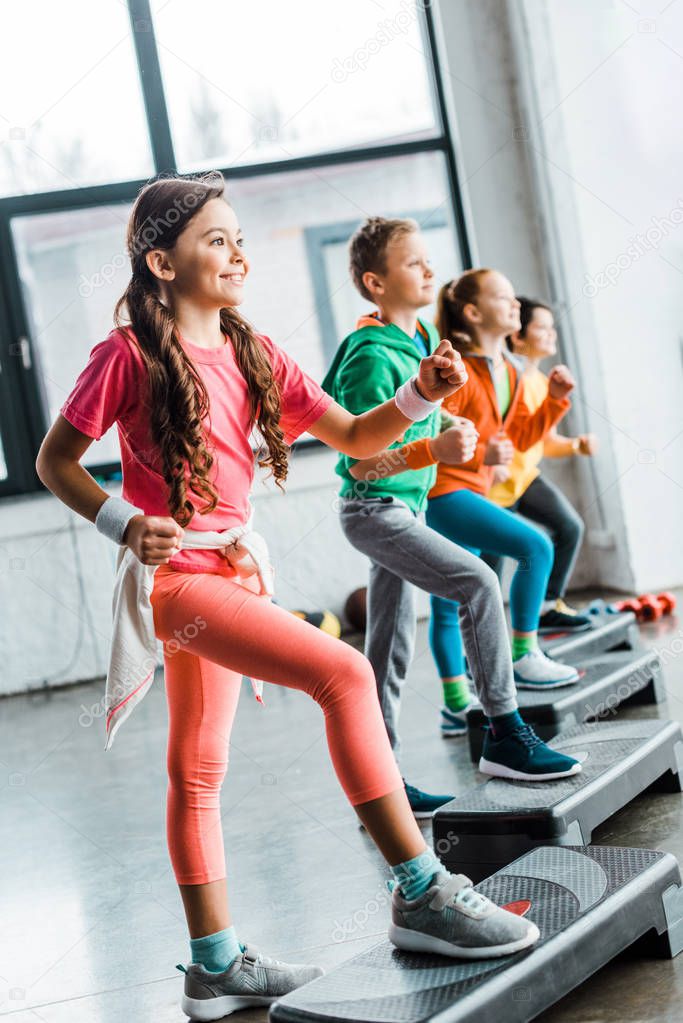 Smiling kids training in gym with step platforms