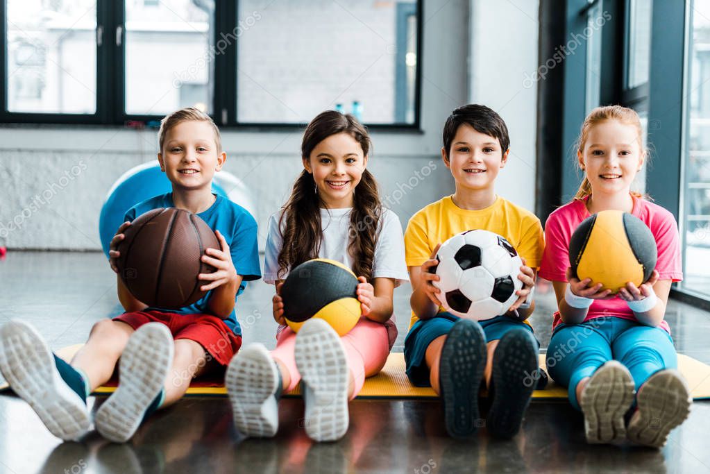 Preteen kids sitting on fitness mat with balls