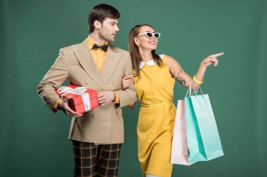 hediye kutusu ve alışveriş torbaları üzerinde yeşil izole tutarken parmak ile işaret kadın vintage giysili adam